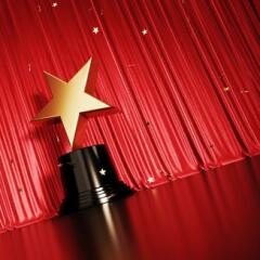 Falling Onto A Gold Star Shaped Award Sitting Before Red Stage Curtain 