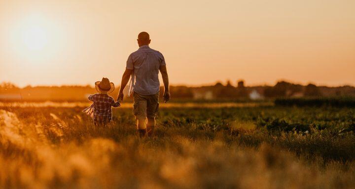 Father and son walking in field at sunset 