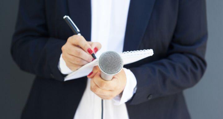 female reporter at a new conference holding a notepad and microphone