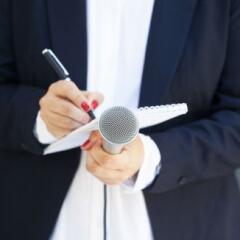 female reporter at a new conference holding a notepad and microphone