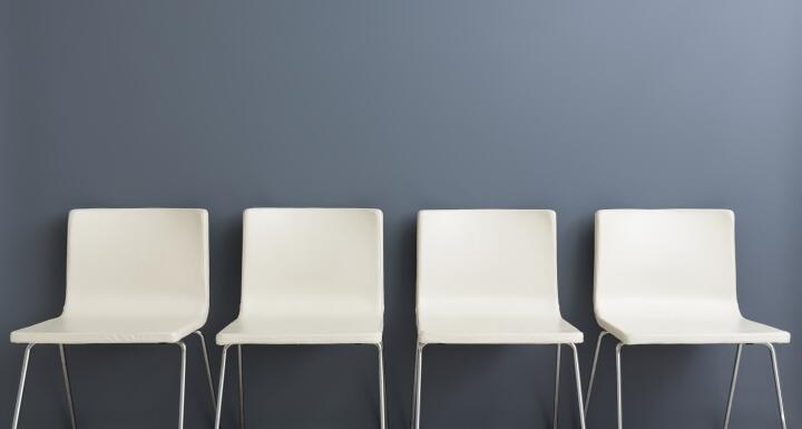 Four modern empty white chairs along a grey wall