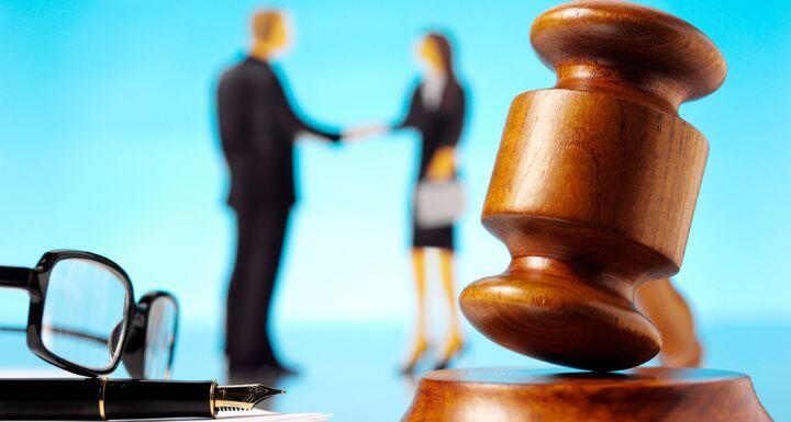 Gavel in the forecment with glasses and paper and a businessman and woman in the background shaking hands