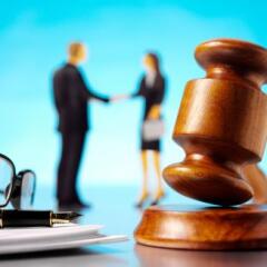 Gavel in the forecment with glasses and paper and a businessman and woman in the background shaking hands