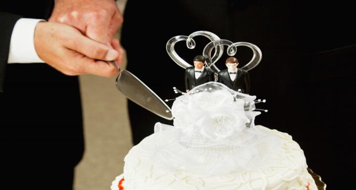 Two grooms cutting white, two-tiered wedding cake