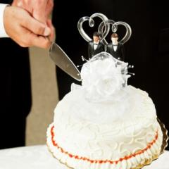 Two grooms cutting white, two-tiered wedding cake