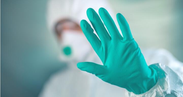 A medical professional wearing head to toe personal protective equipment with a gloved hand held up signaling to stop