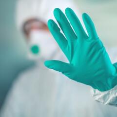 A medical professional wearing head to toe personal protective equipment with a gloved hand held up signaling to stop