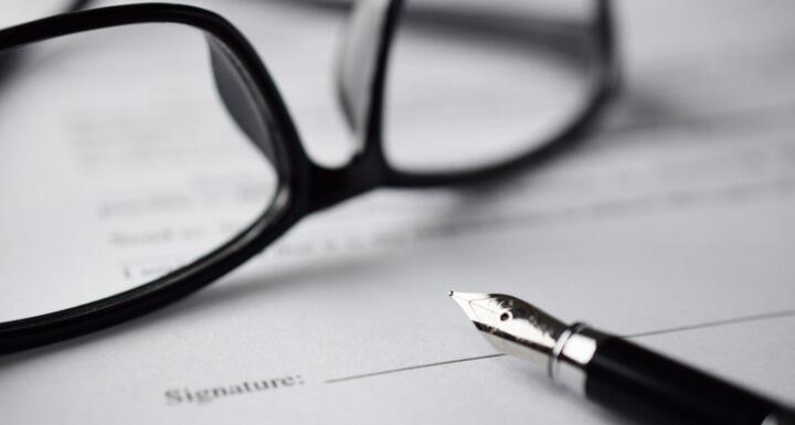 A pair of black glasses and fountain pen on top of a contract