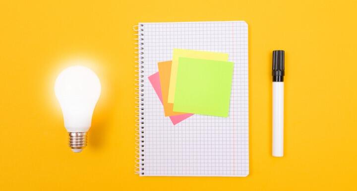 Glowing lightbulb with sticky notes on notepad and pen