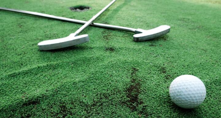 Golf clubs in cross shape with golf ball on green turf