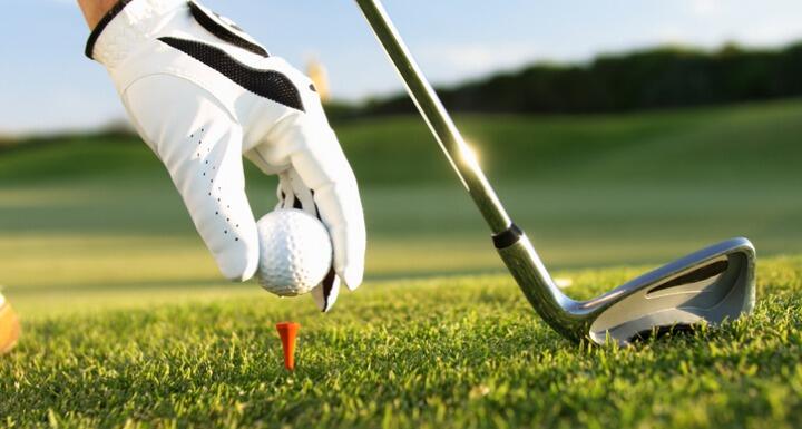 Golfer putting ball on tee with golf club and blue skies in background