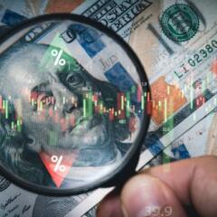 Hand holding magnifier glass to focus Benjamin Franklin face on USD dollar 