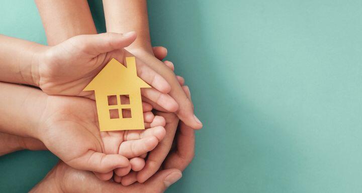 Hands holding yellow paper house on blue background