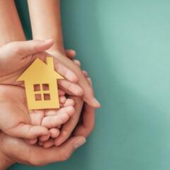 Hands holding yellow paper house on blue background