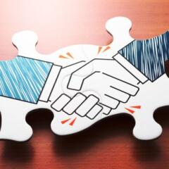 Handshake jigsaw puzzle pieces on wood desk