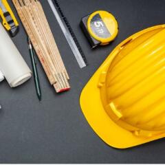 Yellow hard hat blue prints tape measure pen and rulers laying on a black surface