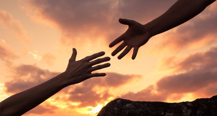 The hands of two people reaching for each other signifying helping hand