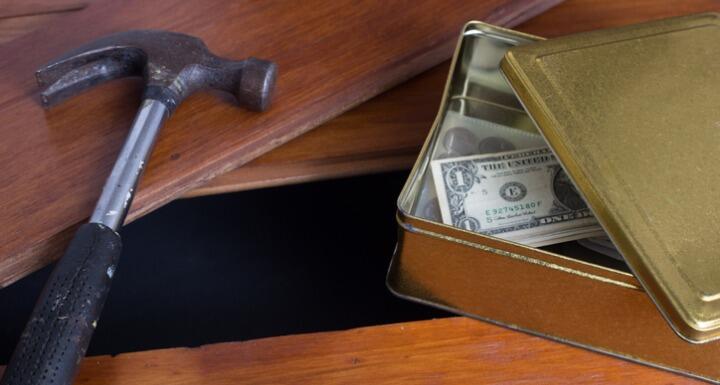 Money in a box with a hammer right beside a hole in a wooden floor