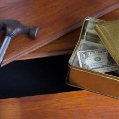 Money in a box with a hammer right beside a hole in a wooden floor