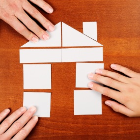 A paper house cut up into piece with hands putting it together