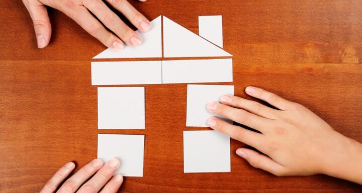 3 hands putting together puzzle shaped as a house