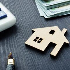 House vale concept with wooden house on table with calculator, money, and pen