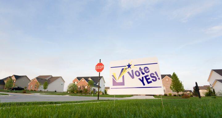 Image of a lawn sign in a neighborhood reading Vote Yes