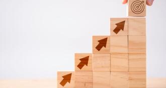 Stacked wooden blocks with arrows leading to a bullseye signifying investments