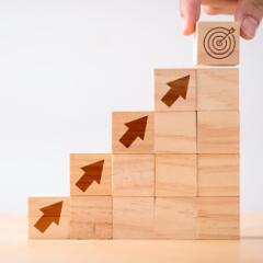 Stacked wooden blocks with arrows leading to a bullseye signifying investments