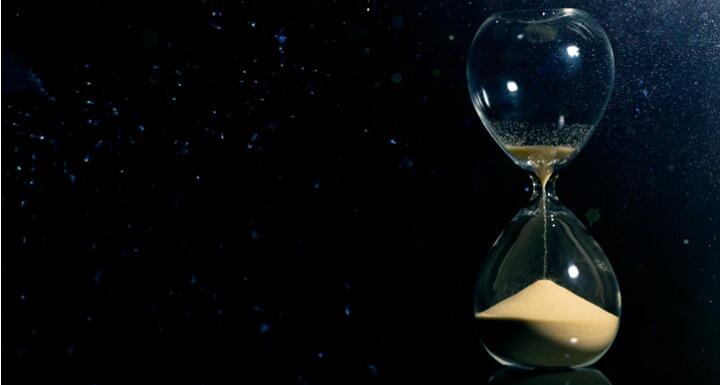 An hourglass on a black background with grains of sand running through it