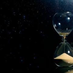 An hourglass on a black background with grains of sand running through it