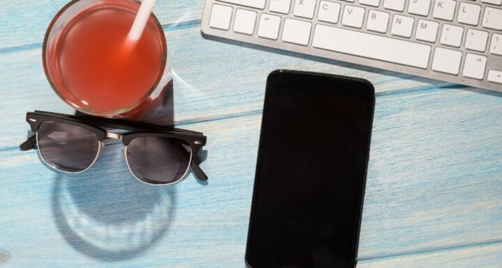 A orange drink, black sunglasses, a cellphone, and keyboard on blue table
