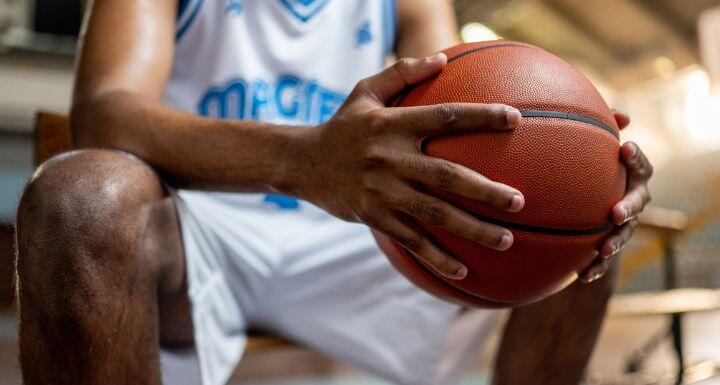 Male basketball player holding ball while sitting on bench