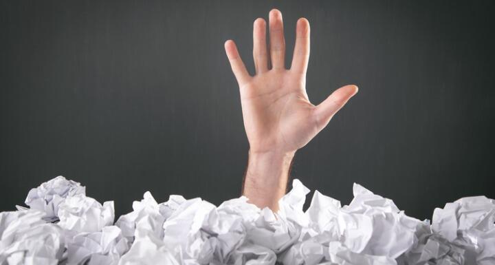 Male hand reaches out from heap of crumpled papers