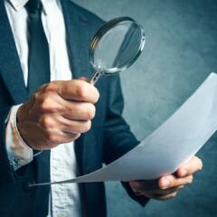 Man in a business suit holding a magnifying glass and reviewing a document