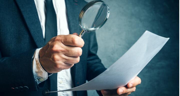 Man in a business suit holding a magnifying glass and reviewing a document