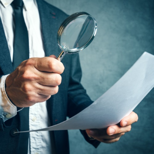 businessman inspecting paper with magnifying glass