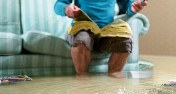 Man sitting in flooded living room using a phone