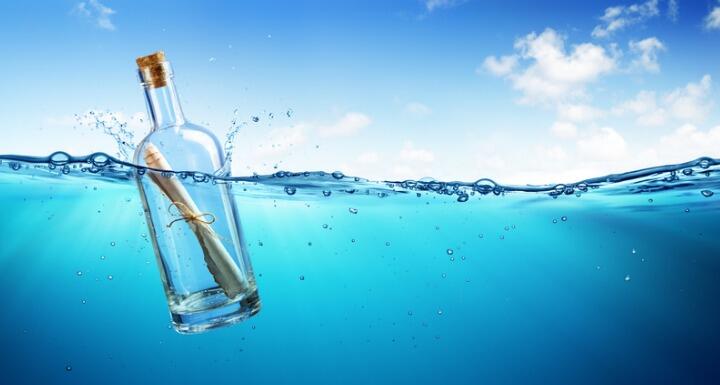 Message in a bottle floating in clear blue water with a clear blue sky in the background