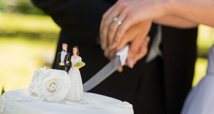 Mid section of a newlywed cutting wedding cake