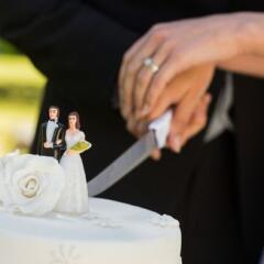 Mid section of a newlywed cutting wedding cake