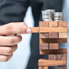 business man playing jenga with coins on the top of the puzzle