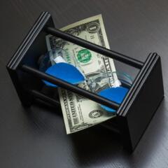 Hour glass with blue sand laying on its side with a one dollar bill weaved into it