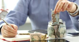 Man putting money in a jar while writing notes
