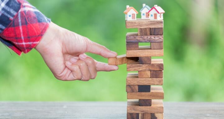 Toy houses on top of Jenga stack as hand pulls out a block