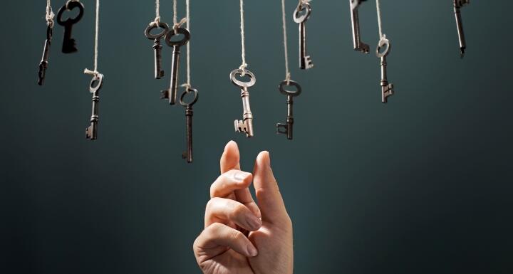 Multiple old fashioned keys hanging in the air on ropes with a hand reaching up and grabbing one