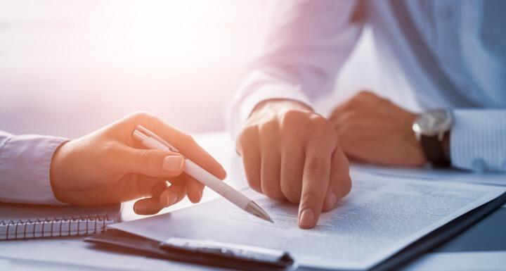 two people pointing at a document on a desk during a negotiation