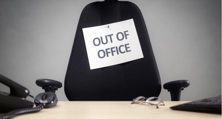 Empty desk chair with out of office sign taped to the back