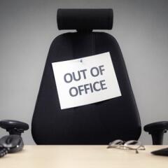 Empty desk chair with out of office sign taped to the back
