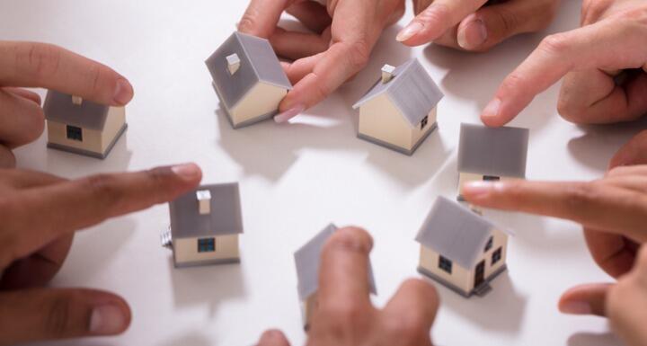 Hands moving mini homes around a white surface